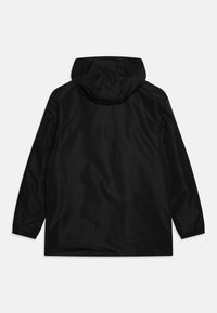 Chaqueta con capucha negra, impermeable, de manga larga y con puños elásticos, vista desde la parte trasera sobre un fondo blanco.