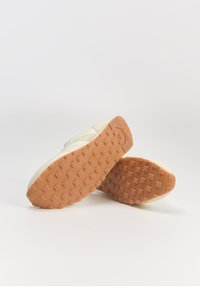 Sneakers z kremową cholewką, teksturowanym materiałem i gumową podeszwą z diamentowym wzorem zapewniającym przyczepność. Dwa buty pokazane od tyłu.