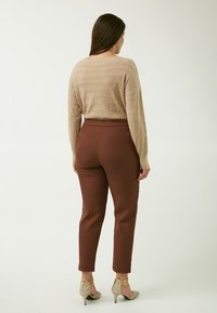Maglione beige a maglia testurizzata con maniche lunghe abbinato a pantaloni marroni aderenti. La modella indossa scarpe con tacco di colore chiaro con accenti dorati.