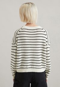 Cremfarbener Pullover mit schwarzen Streifen, langen Ärmeln und geripptem Ausschnitt. Weicher, strukturierter Stoff mit lockerer Passform und sichtbaren Nahtdetails.