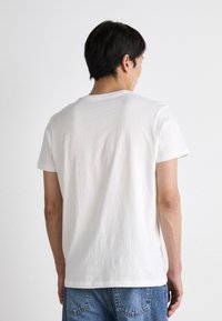 Hvit bomulls t-skjorte med korte ermer, rund hals og glatt tekstur, iført med blå denimjeans, sett fra baksiden.