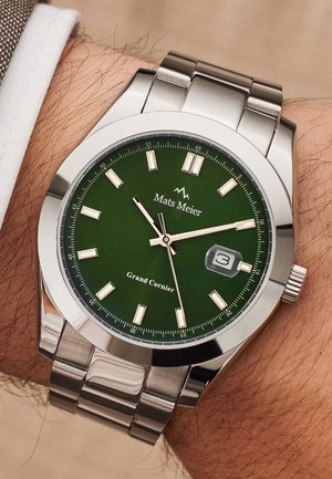 Montre en acier inoxydable avec un cadran vert, des index horaires dorés et un affichage de la date. Elle dispose d'un bracelet métallique et d'une couronne sur le côté.