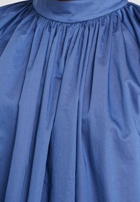 Jupe en tissu bleu froncé avec une large ceinture, de doux plis créant une silhouette volumineuse et fluide.