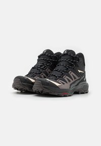 Chaussures de randonnée noires et beige avec tige en textile, semelles en caoutchouc et système de laçage visible. Présentent un motif en relief pour une meilleure traction.