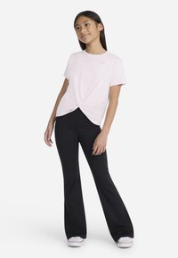 T-shirt rose à manches courtes avec un nœud à l'avant, associé à un pantalon noir évasé et des chaussures blanches. Tenue simple et décontractée.