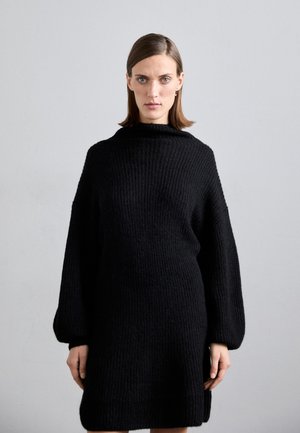 Black knitted dress with a high neckline, oversized sleeves, and a textured pattern, extending to mid-thigh with side slits.