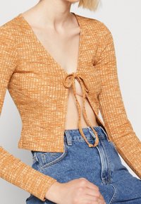 Orange texturerad stickad kort cardigan med v-ringning och knytfront, i kombination med högmidjade blå denimjeans.