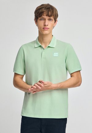 Mintgrøn polo t-shirt med krave, korte ærmer og en subtil stribe detalje. Har et rektangulært logo-patch på brystet. Blød tekstur.