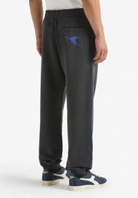 Pantaloni della tuta grigio scuro con strisce laterali blu, polsini elastici, una tasca posteriore e dettagli con logo. Realizzati in materiale morbido per il massimo comfort.