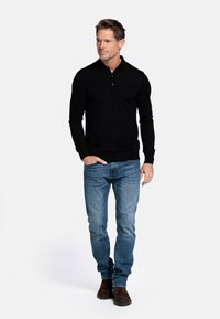 Zwart poloshirt met lange mouwen en kraag, voorzien van drie knopen, gecombineerd met blauwe jeans en bruine suède laarzen. Eenvoudig, strak ontwerp.