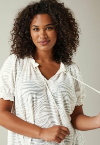 Weiße Bluse mit einem strukturierten Zebra-Muster, kurzen Puffärmeln und einem V-Ausschnitt. Der Stoff wirkt leicht und leicht transparent.