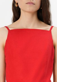 Top rosso senza maniche con scollatura quadrata, realizzato in tessuto testurizzato; con spalline sottili e un design aderente.