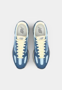 Blue and light blue sneakers with yellow laces, textured suede and mesh materials, rounded shape, and rubber sole. New Balance logo on the insole.