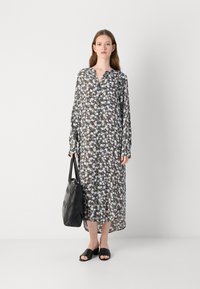 Lungo vestito floreale con un design a bottoni e scollatura a V, nei motivi nero, bianco e viola. Abbinato a una borsa nera e sandali.