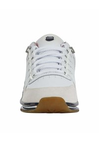 Vita idrottssko med en slät läderoversida, mockadetaljer, nätkrage och gummisula. Har silverfärgade ögla och en logotyp på kragen.