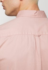 Camisa de manga corta de color rosa claro con cuello clásico, detalle de canesú en la espalda y tela de algodón suave con textura lisa.