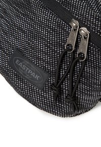 Černobílá texturovaná látka batohu se zipovým uzavíráním, s nerezovými zipy a černou gumovou nášivkou Eastpak.