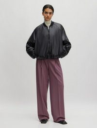 Zwarte satijnen bomberjack met een ritssluiting, geribbelde manchetten en zoom, gecombineerd met hoge, wijde mauve broeken en zwarte hakken.