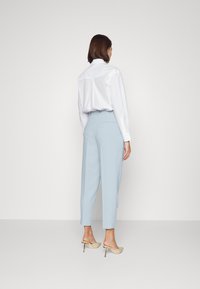 Light blue high-waisted pants paired with a white button-up shirt, featuring long sleeves and a back pleat, complemented by beige heeled sandals.