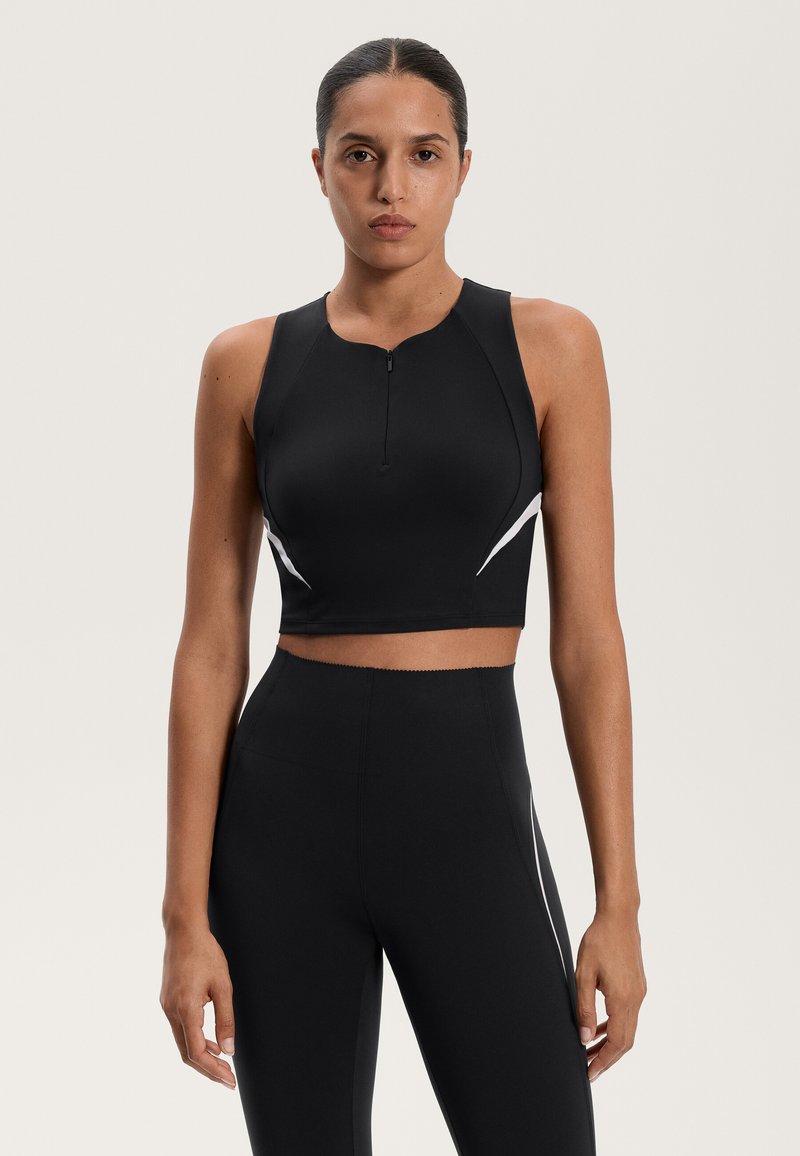 Čierny športový crop top s vysokým golierom, predným zipsom a bielymi akcentmi. Vyrobený z hladkého, priliehavého materiálu, navrhnutý na aktívne nosenie.