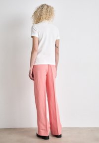Bílá krátký rukáv polo tričko spárované s volně padnoucími, světle růžovými kalhotami. Tento outfit má neformální design s uvolněným střihem a minimálními detaily.