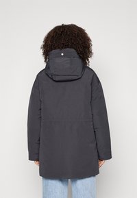 Mörkgrå puffjacka med huva, ribbad krage och rak passform. Har en slät textur och minimala metalldetaljer.