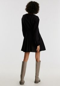 Robe noire longueur genou avec manches longues et taille cintrée. Modèle assorti avec des bottes grises claires montant jusqu'au genou. Texture de tissu lisse.