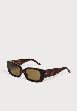 Lunettes de soleil rectangulaires en écaille de tortue avec des verres marron foncé et des branches épaisses légèrement inclinées sur fond blanc.