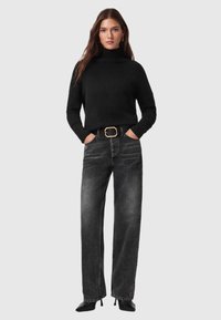 Suéter negro de punto con cuello alto combinado con jeans oscuros de pierna recta y cintura alta. La modelo lleva un cinturón negro con detalles dorados.