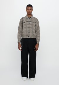 Woven, cropped jacket in multicolored fabric with a button closure, black accents, and a pointed collar, paired with black pants and white sneakers.
