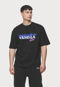 Juodas marškinėliai trumpomis rankovėmis su daugiakalbe grafine tekstų dizainu: "pegador VANILLA Super Soft!" mėlynos ir rožinės spalvų.