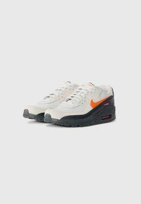 Kremaste i crne atletske tenisice s narančastim Swoosh logom, gornjište od teksturirane tkanine, podloga s amortizacijom i detalj sa zračnom amortizacijom.