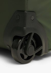 Rueda negra unida a una maleta verde con una superficie texturada; destaca el diseño circular y los accesorios de plástico robustos.