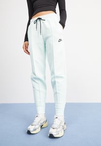 Lichtblauwe joggingbroek met een trekkoord in de taille, zijzakken en een zwart Nike-logo. Gecombineerd met zilveren en crèmekleurige Nike-sneakers.