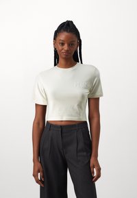 Ljust beige kortärmad t-shirt med präglad textdetalj. Matchas med mörkgrå, veckade hög midja-byxor.