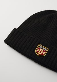 Zwarte gebreide beanie met ribbeltextuur en omgeslagen rand. Bevat een kleurcontrasterend geborduurd label met "GANT" en het jaar "1949."