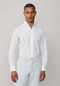 Camisa blanca de manga larga con cierre de botones, que presenta un acento en azul claro en el interior del cuello, combinada con pantalones azul claro.