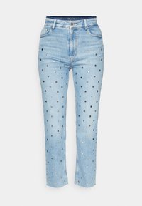 Jean en denim bleu clair avec des clous métalliques circulaires argentés et noirs répartis uniformément sur le devant, avec un ourlet brut et un design classique à cinq poches.