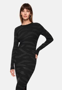 Black long-sleeve rib-knit dress featuring a textured wavy pattern, slim fit, and side slit, with a round neckline.