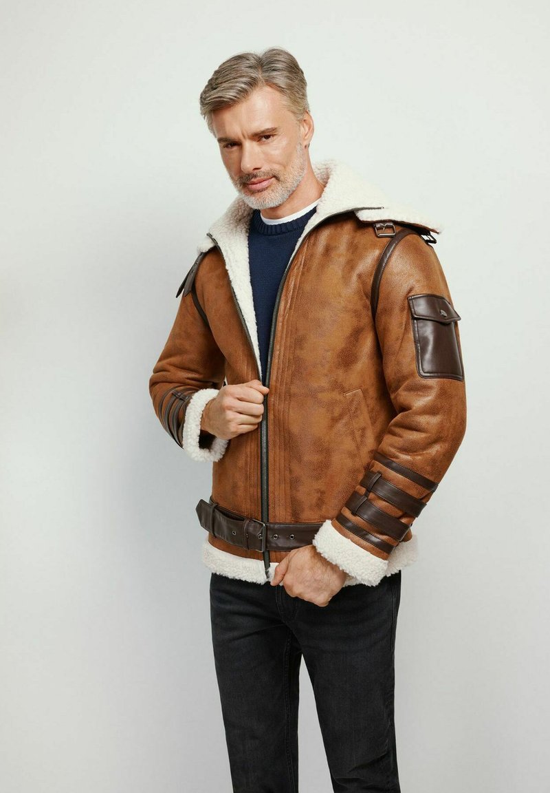 Giacca in finta pelle marrone con colletto in shearling bianco, chiusura con zip e dettagli scuri. Presenta spalline e dettagli a coste sulle maniche.