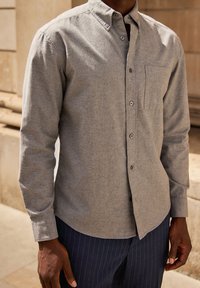 Grijze button-up shirt van een textuurstof, met een borstzak en een gebogen zoom. Gestyleerd met marineblauwe broek met streepjes.