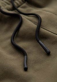 Tissu vert olive avec une texture douce, doté de cordons noirs avec des embouts en plastique, mettant en avant un design simple mais fonctionnel.