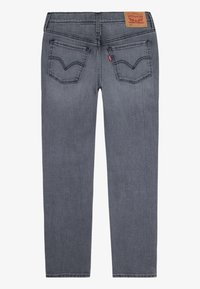 Vue arrière d'un jean Levi's gris avec deux poches arrière, surpiqûres arcuates caractéristiques, étiquette rouge Levi's, et patch en cuir marron de la marque sur la ceinture.
