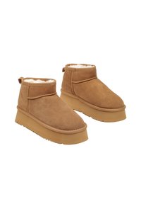 Bottines en suede tan avec une doublure douce et texturée, présentant une semelle plateforme épaisse et un design simple à revers.