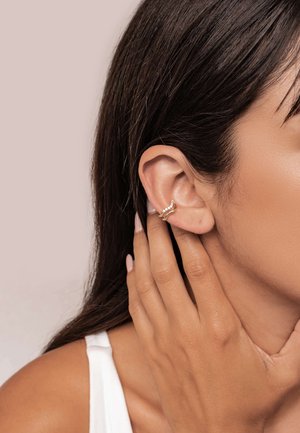 Goldfarbiger Ohr-Cuff mit wellenförmigem Design, versehen mit kleinen eingearbeiteten Kristallen, der am oberen Ohr getragen wird. Glatte Textur, minimalistischer Stil.