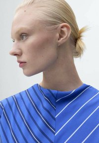 Vêtement bleu avec des rayures blanches en diagonale ; tissu doux avec une texture lisse ; présente un col haut et une silhouette décontractée et drapée.