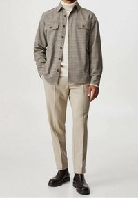 Camicia a quadri in beige e marrone, abbinata a pantaloni tapered beige chiaro e stivaletti marrone. Tessuto morbido e vestibilità su misura.