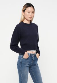 Marinblå kort tröja med lång ärm och rund halsringning; strukturerad stickad tyg kombinerad med ljusblå skinny jeans.