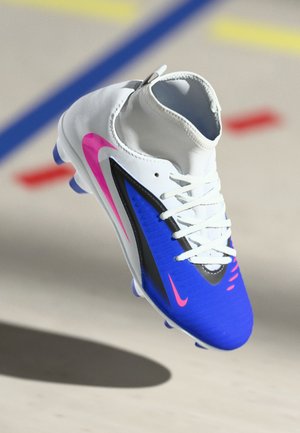Crampons de football Nike blancs, bleus et roses avec lacets, flottant au-dessus d'un sol marqué de lignes colorées.