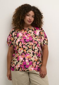 Blommig blus med korta puffärmar, som har en svart bakgrund och livfulla mönster av rosa, orange och neutrala blommor.